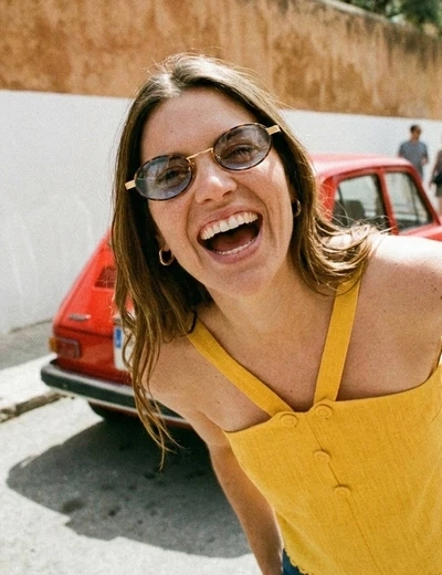 Femme en robe jaune qui sourit devant une voiture rouge